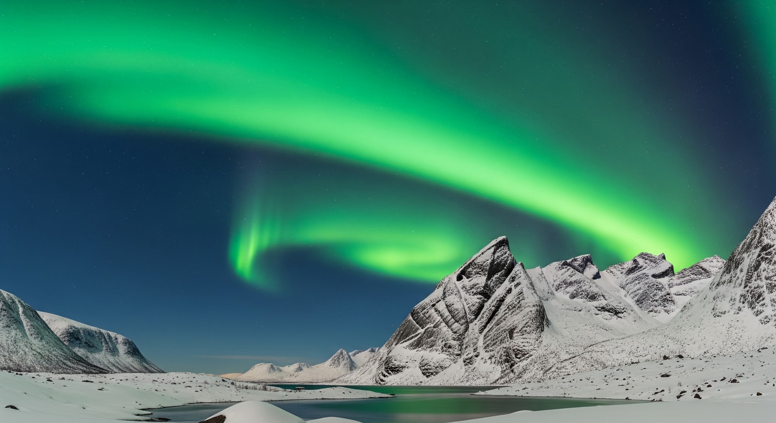 Vibrant green Northern Lights aurora borealis dancing over snow-covered mountains in Tromso