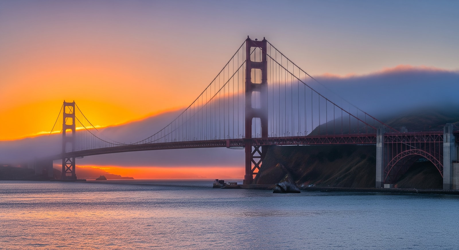 The iconic Golden Gate Bridge spanning San Francisco Bay at sunset with fog rolling through the towers